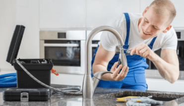 Man in blue overalls adjusting sink faucet