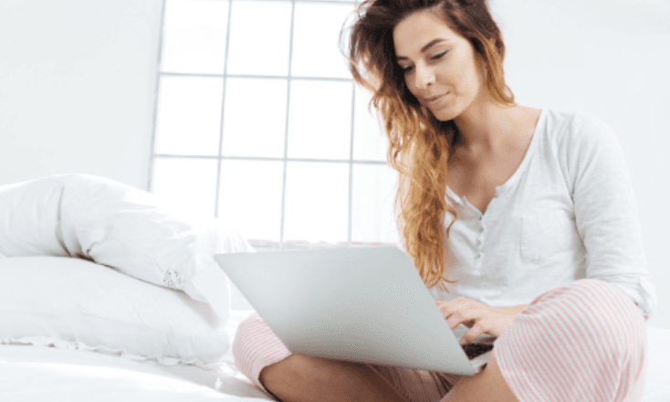 Woman sitting on her bed looking at laptop